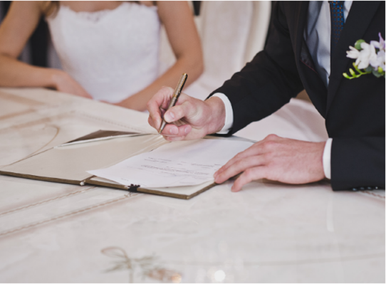 Married couple in wedding clothes signing document